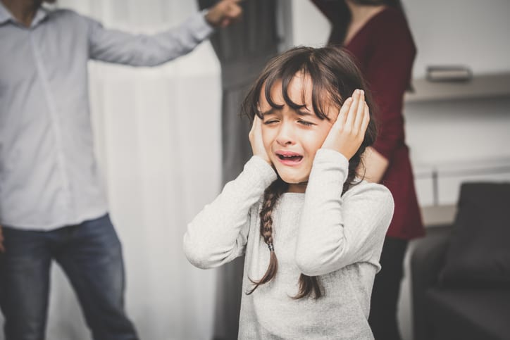 Child in distress with hands over her ears, parents fighting